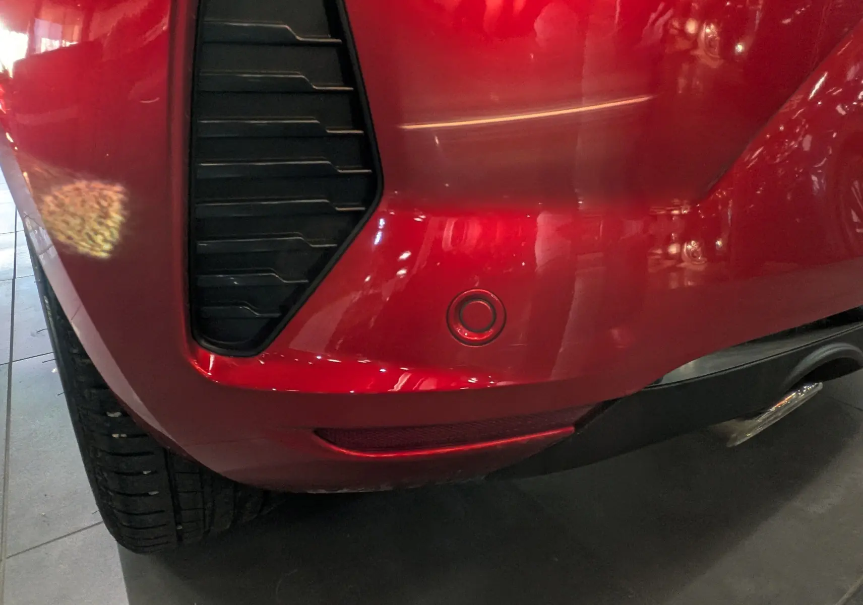 Gros plan sur le pare-chocs arrière droit rouge flamme de la Renault Clio V avec capteur de recul et diffuseur noir.