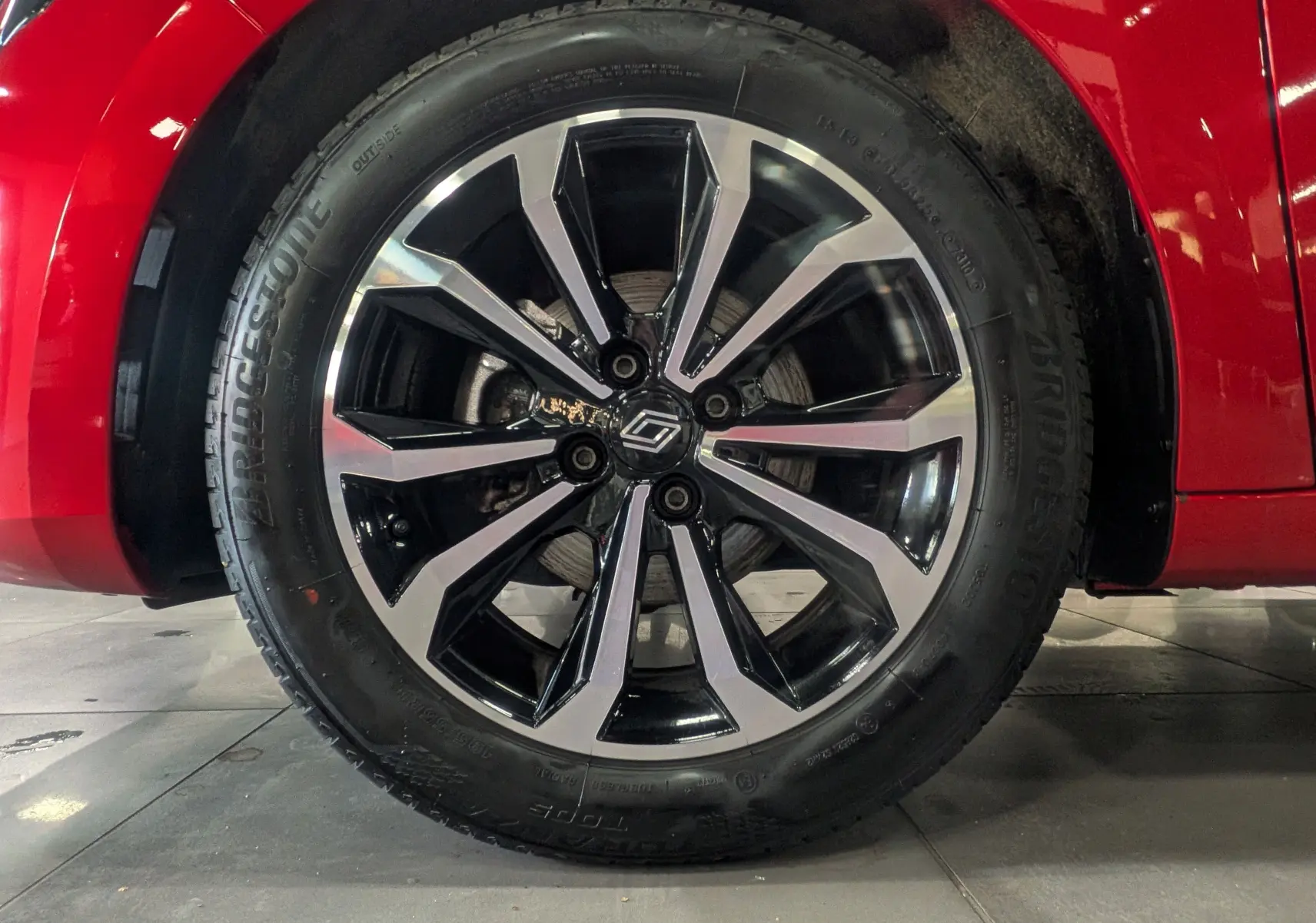 Gros plan sur la roue avant gauche de la Renault Clio V Rouge Flamme avec jante alliage bicolore au design moderne.