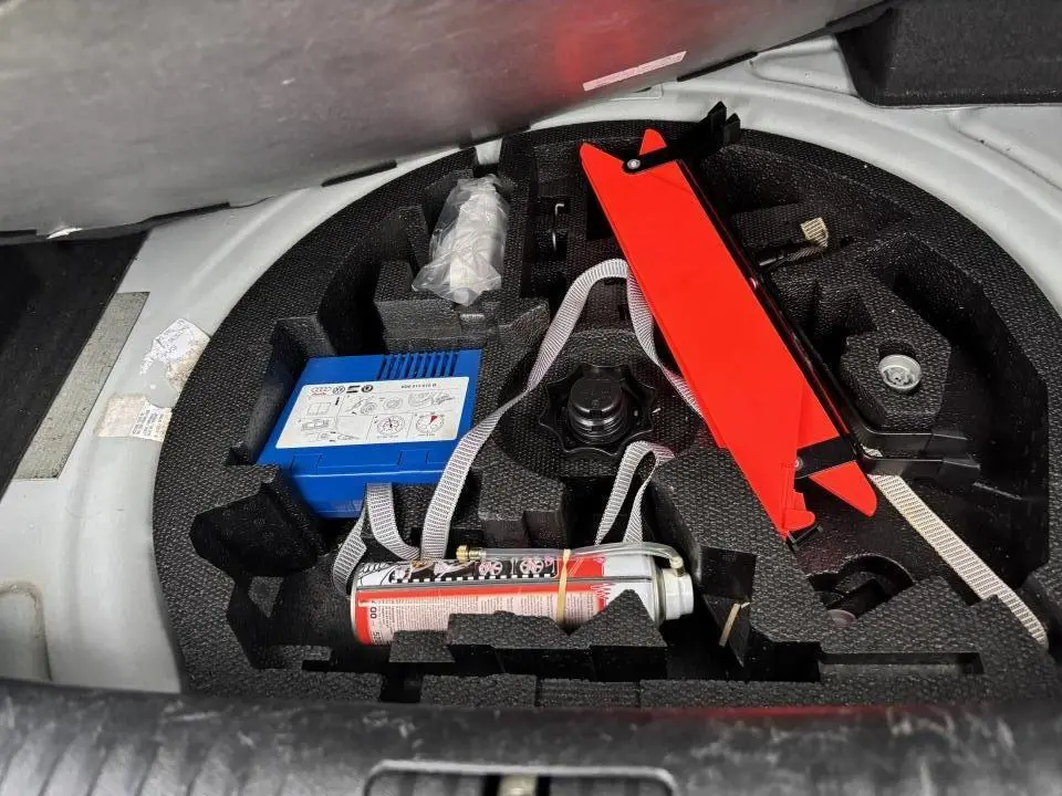 Coffre ouvert d'une Volkswagen Golf VI Cabriolet blanc, vue sur le kit de réparation pneu avec compresseur et cric rouge.