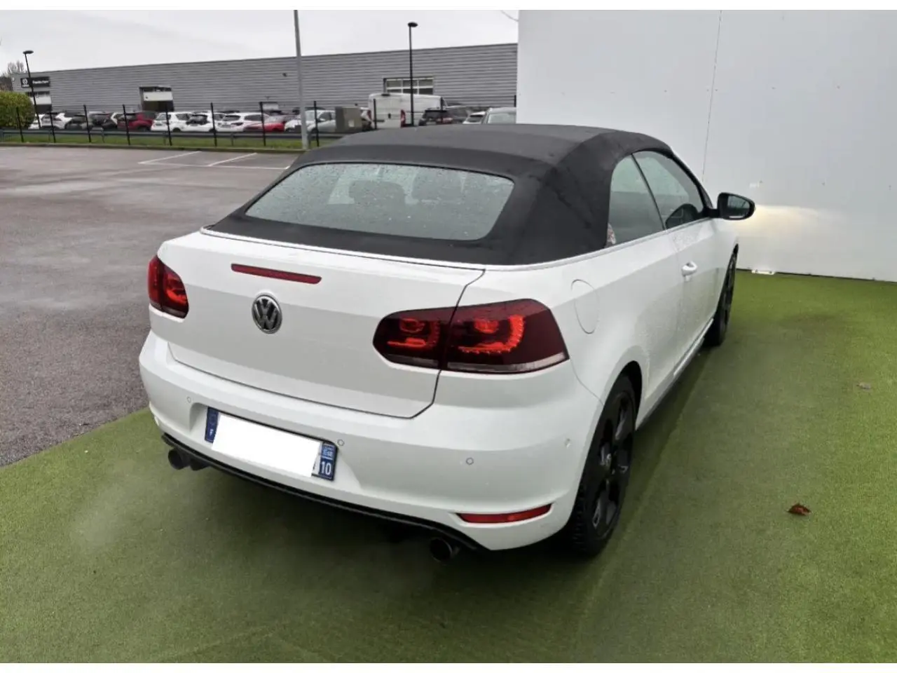 Vue 3/4 arrière droite d'une Volkswagen Golf VI Cabriolet blanche avec toit souple noir et feux arrière LED teintés.