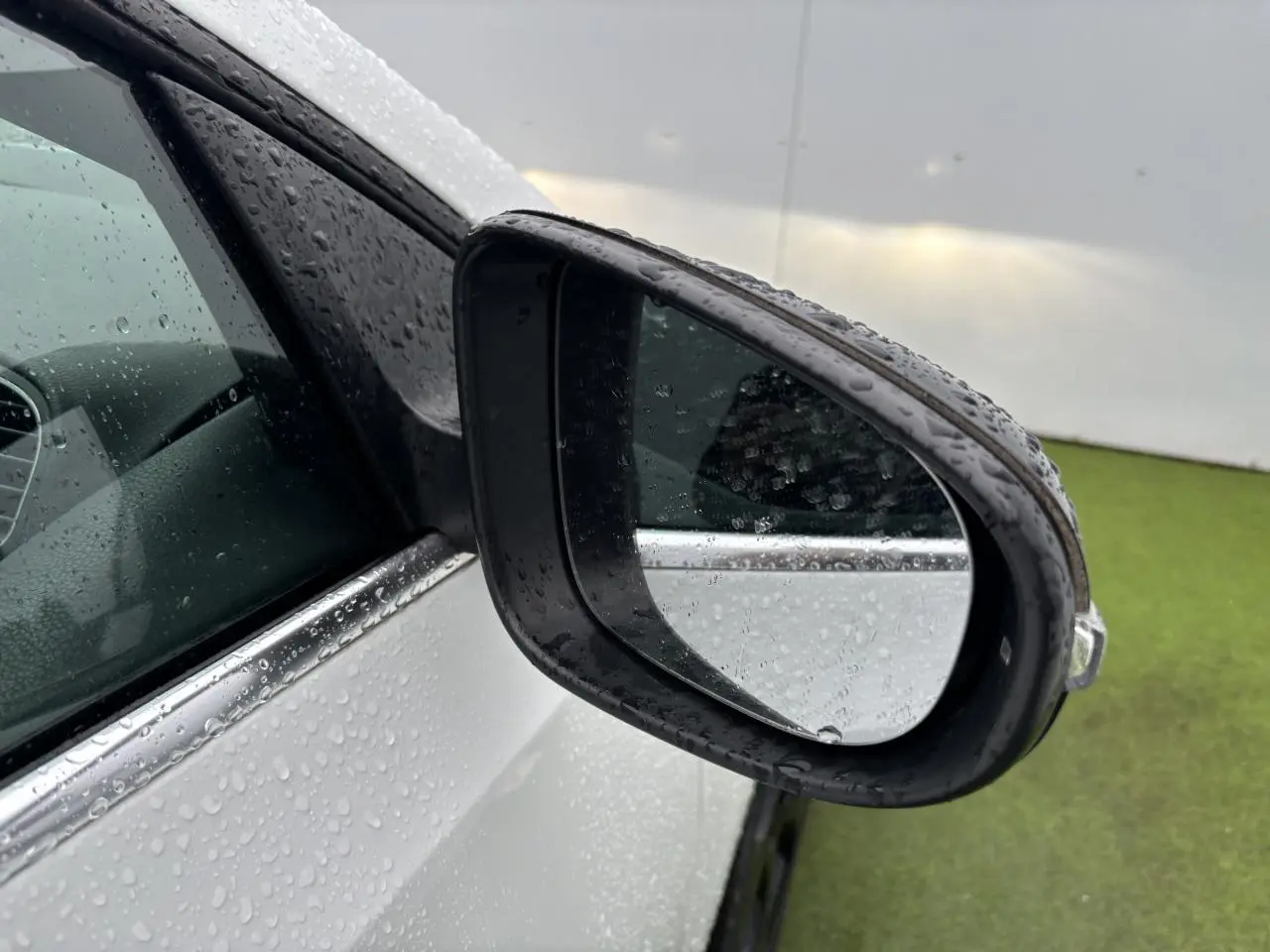 Rétroviseur côté gauche d'une Volkswagen Golf VI Cabriolet blanc avec gouttes de pluie sur la carrosserie et vitre teintée.