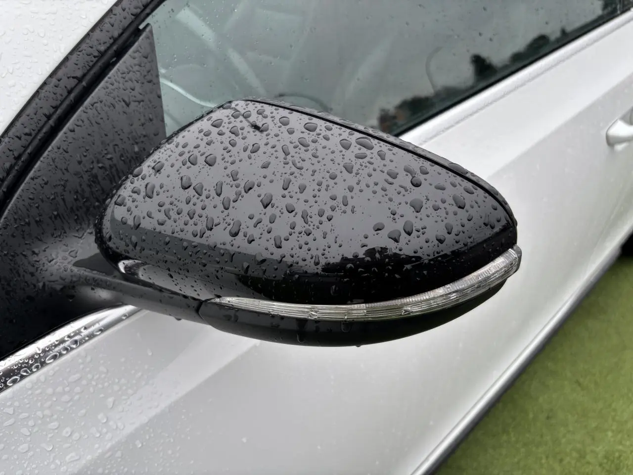 Rétroviseur noir côté gauche avec clignotant intégré sur Volkswagen Golf VI Cabriolet blanc, vue rapprochée sous la pluie.