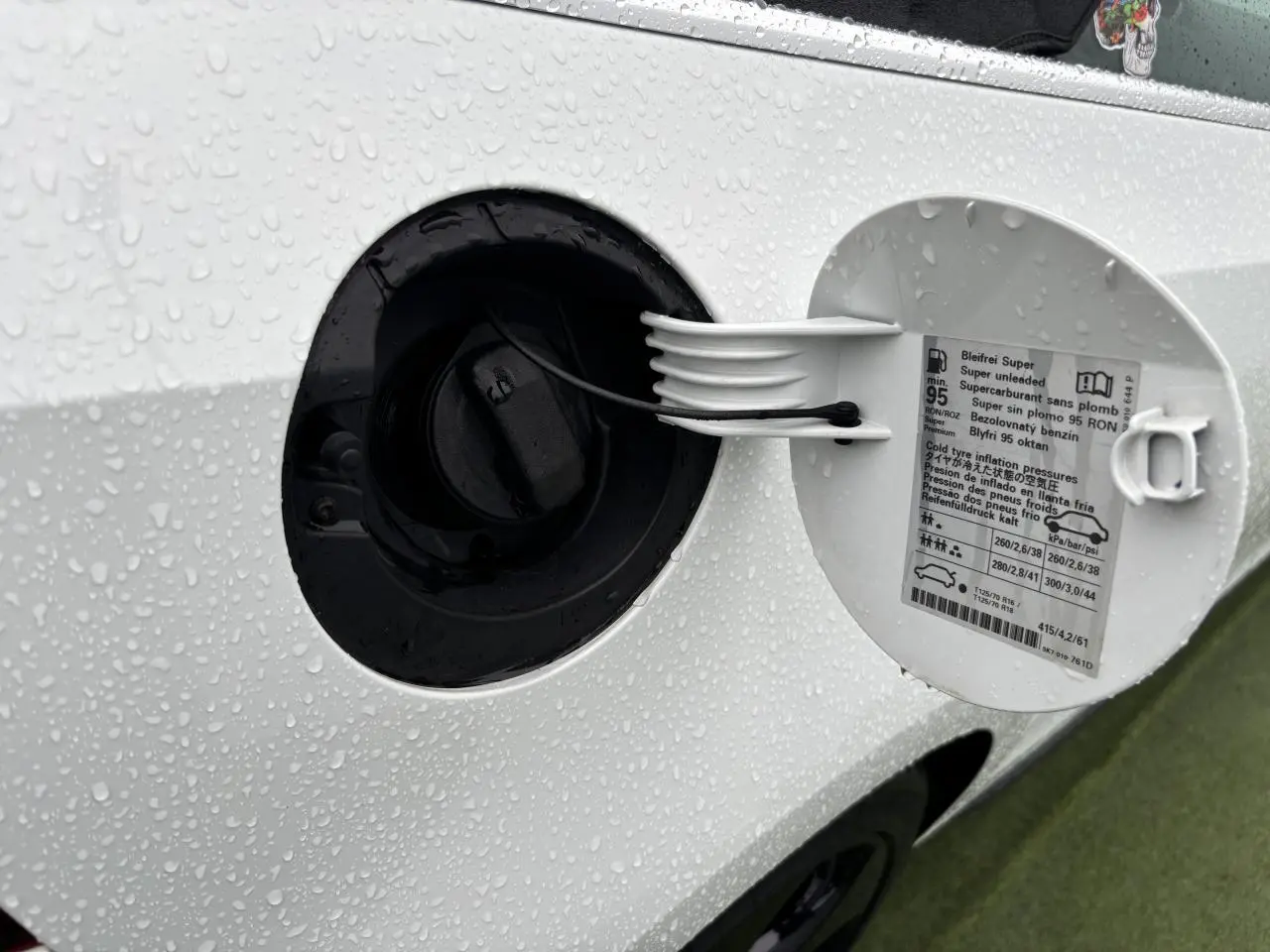 Détail de la trappe à carburant ouverte sur une Volkswagen Golf VI Cabriolet blanche, avec gouttes d'eau visibles.