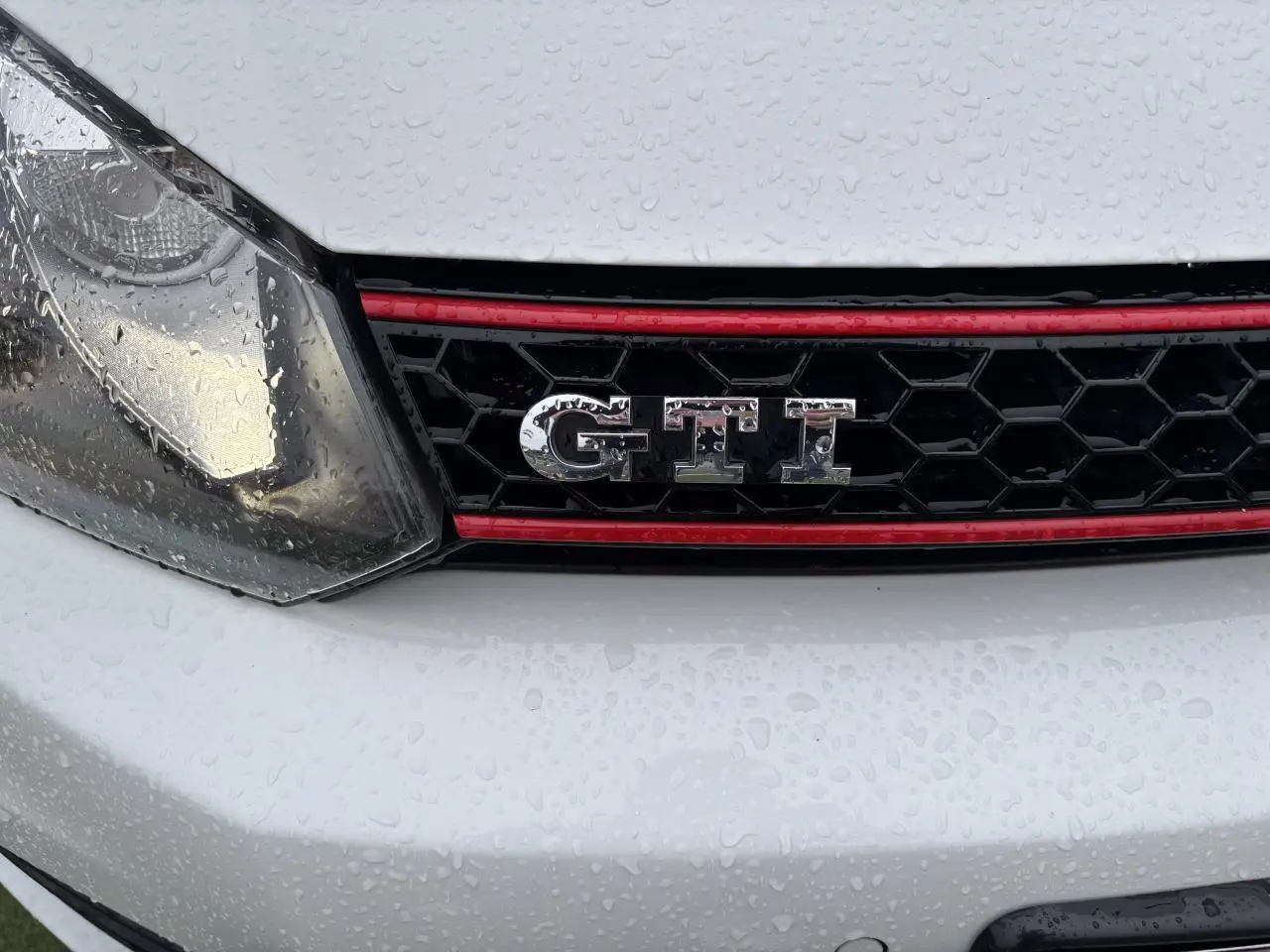 Gros plan sur la calandre avant blanche d'une Volkswagen Golf VI Cabriolet GTI avec logo GTI et liseré rouge.
