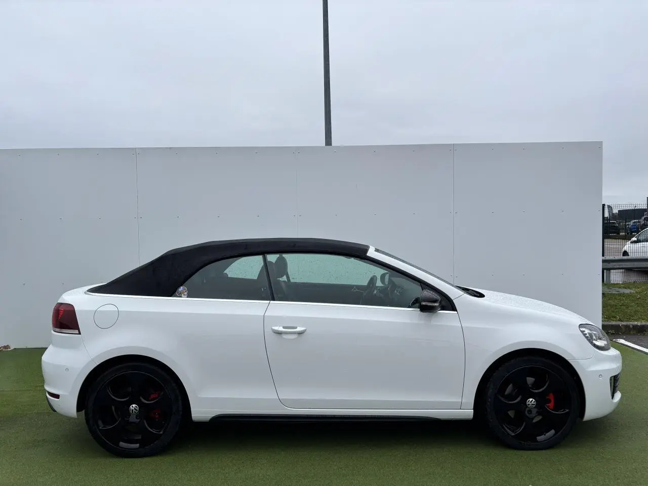 Profil droit d'une Volkswagen Golf VI Cabriolet blanche avec toit souple noir et jantes alliage noires.