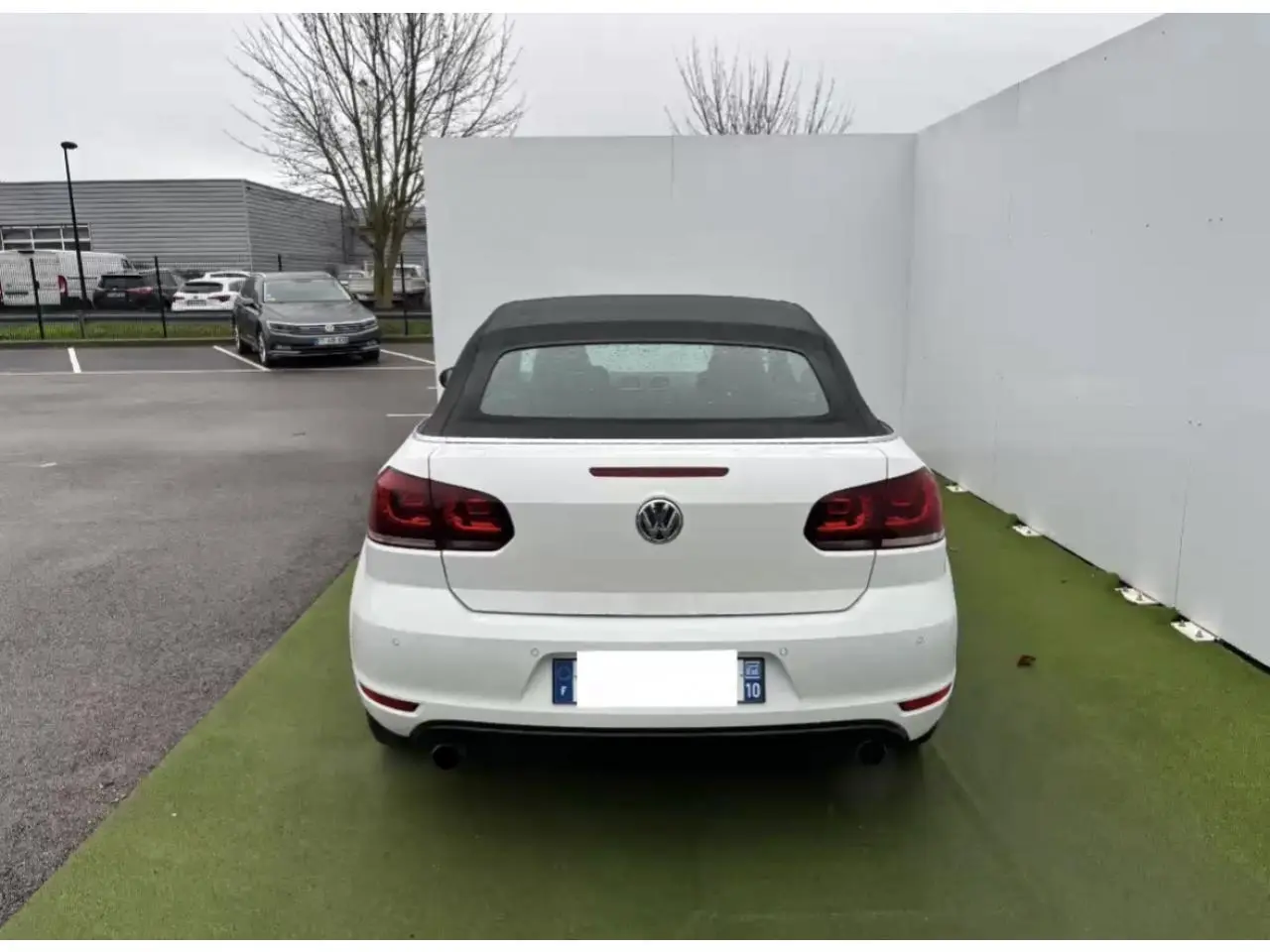 Vue arrière d'une Volkswagen Golf VI Cabriolet blanche avec toit souple noir et feux arrière teintés à LED.