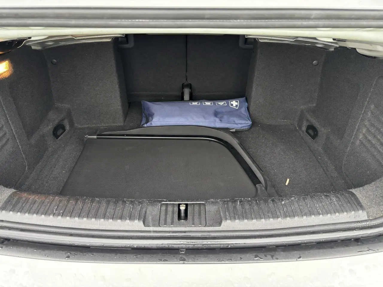 Coffre ouvert d'une Volkswagen Golf VI Cabriolet blanche, montrant un filet de séparation et une trousse de secours bleue.