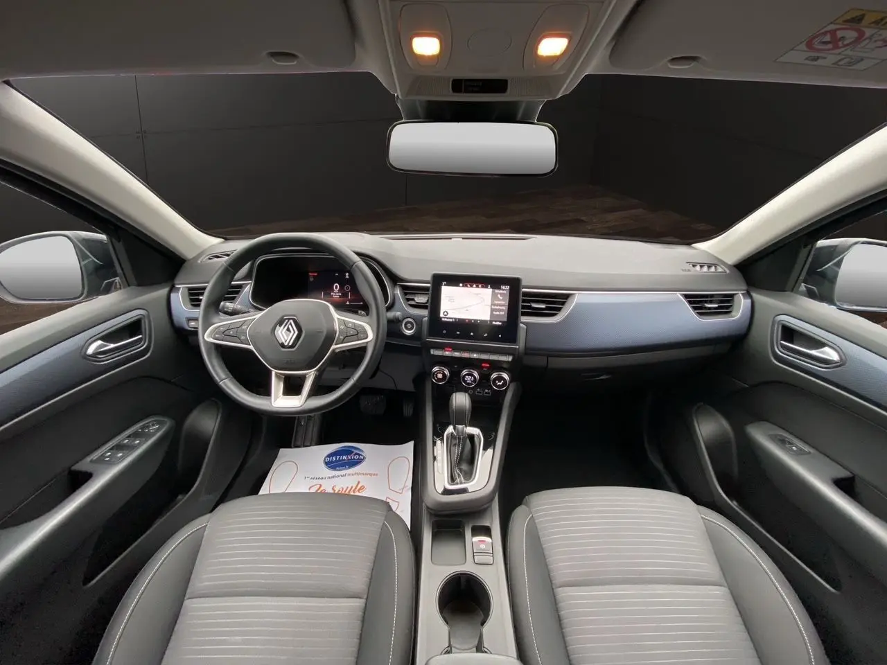 Vue intérieure avant de la Renault Arkana 2024, tableau de bord moderne avec écran tactile et volant multifonction noir.