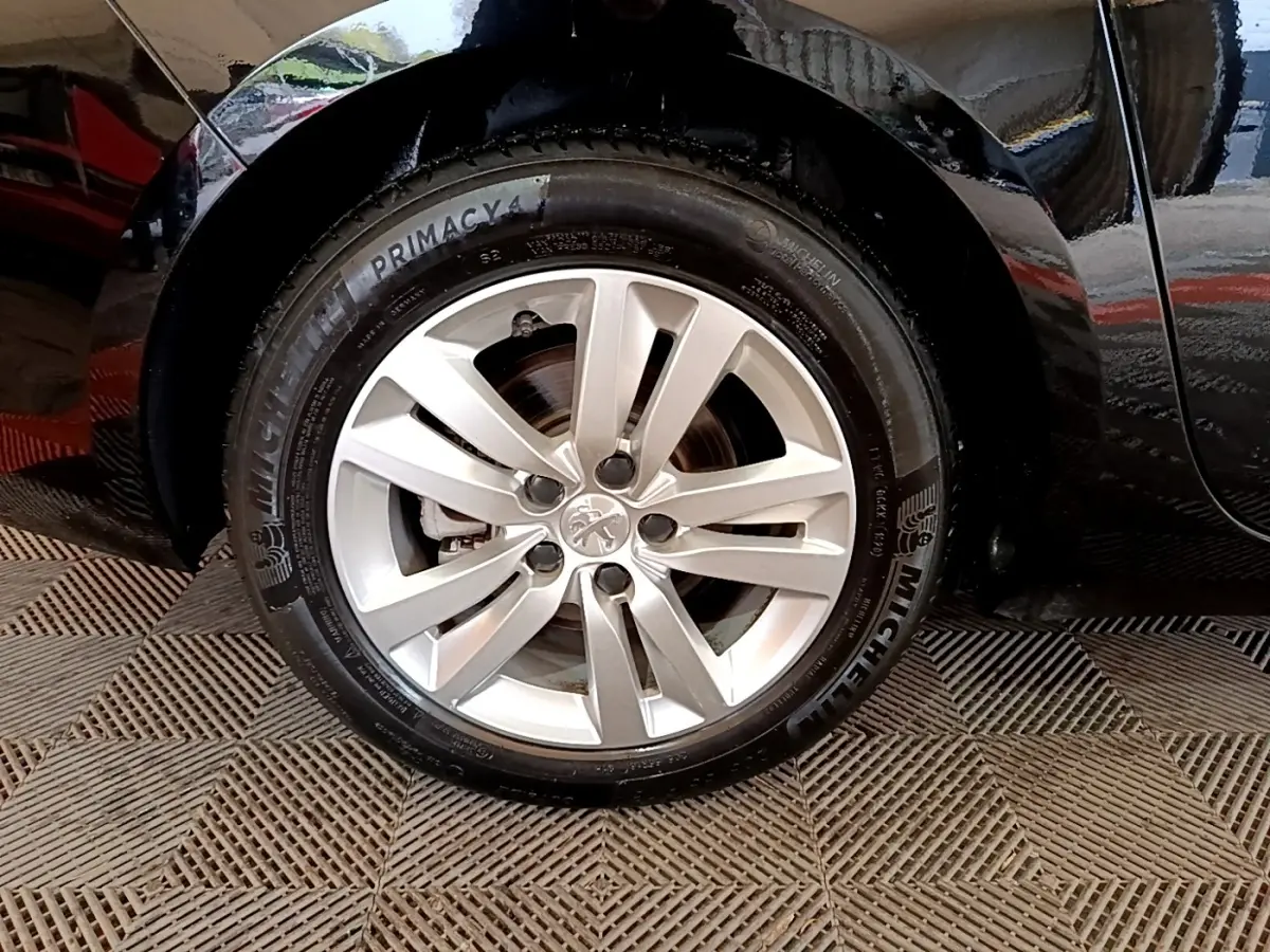 Gros plan sur la roue avant gauche d’une Peugeot 308 noire, mettant en valeur la jante alliage et le pneu Michelin.