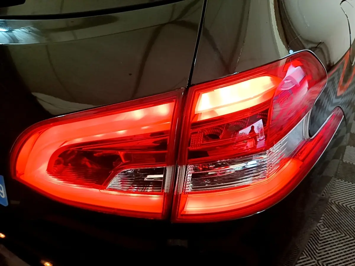 Gros plan sur le feu arrière droit rouge allumé d'une Peugeot 308 noire, reflet sur la carrosserie brillante.