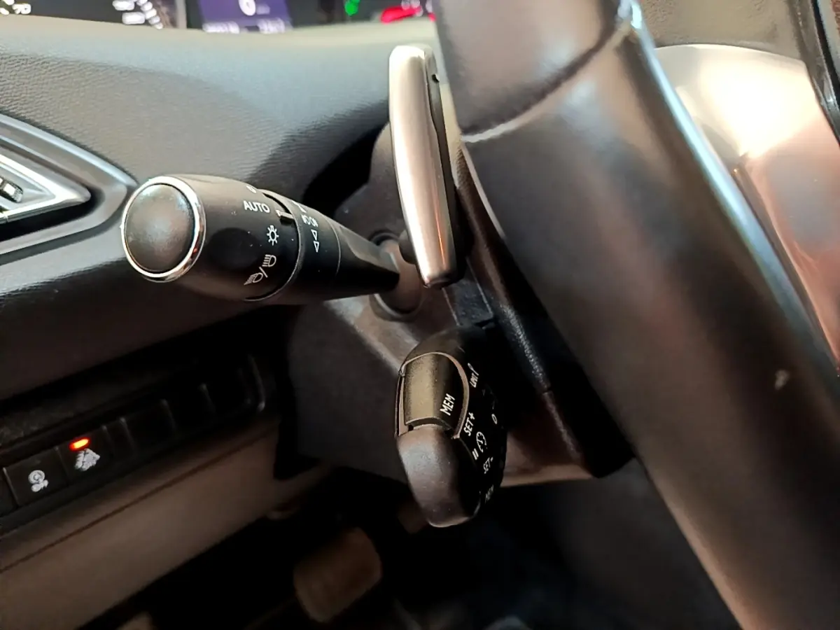 Gros plan sur les commandes au volant côté gauche d’une Peugeot 308 noire, avec leviers de clignotants et régulateur de vitesse.