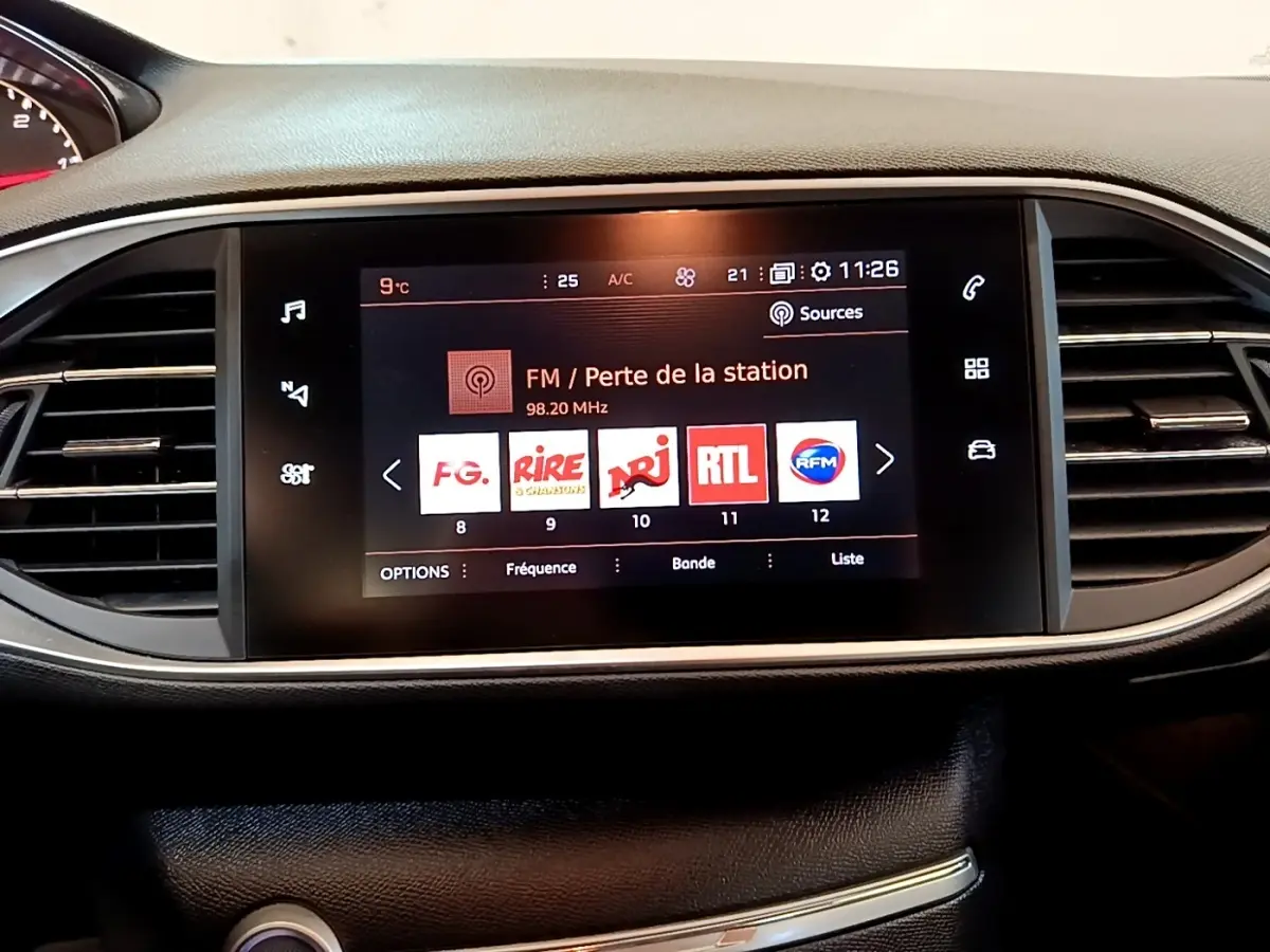 Vue rapprochée de l’écran tactile central du tableau de bord de la Peugeot 308 noire, affichant les stations radio FM.