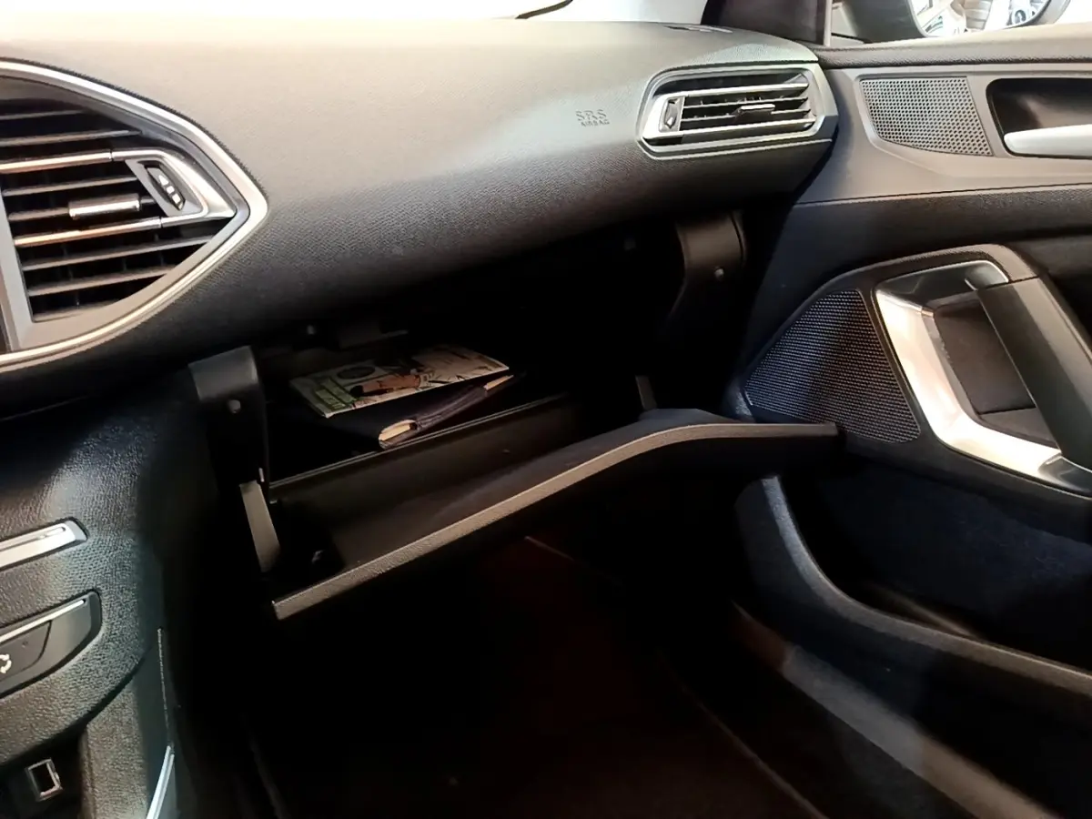 Vue intérieure côté passager de la Peugeot 308 2020, boîte à gants ouverte avec documents visibles, ambiance noire.