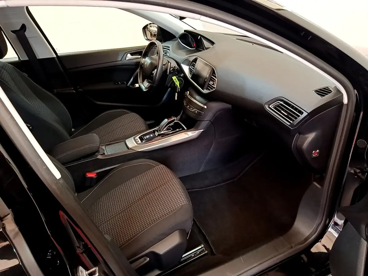 Intérieur avant droit de la Peugeot 308 noire, montrant sièges tissu, tableau de bord et console centrale avec boîte auto.