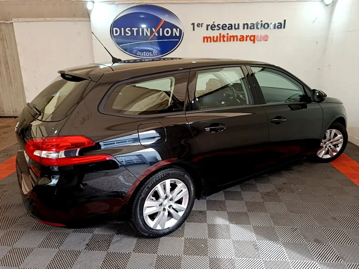 Peugeot 308 noir vue 3/4 arrière droit, avec feux arrière rouges et jantes argentées dans un showroom.