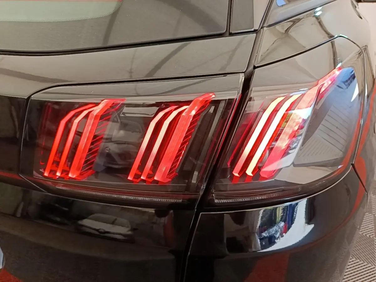 Gros plan sur les feux arrière rouges du Peugeot 3008 noir, vue de l'arrière droite avec reflets sur la carrosserie.