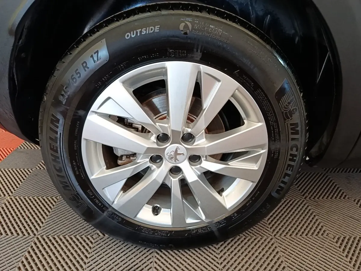 Gros plan sur la roue avant droite d’un Peugeot 3008 noir, jante alliage argentée avec logo Peugeot central.