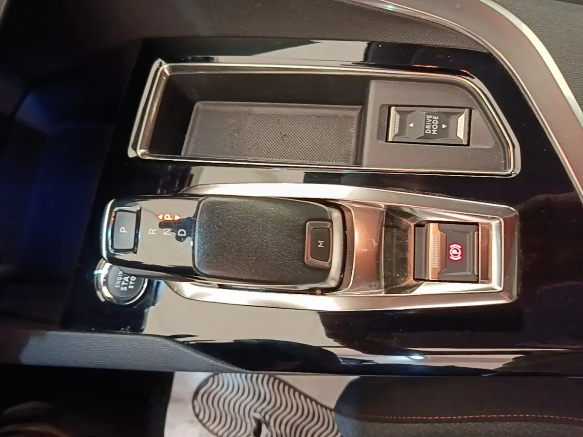 Gros plan sur la console centrale noire du Peugeot 3008 2022, avec levier de boîte auto et bouton frein électrique allumé.