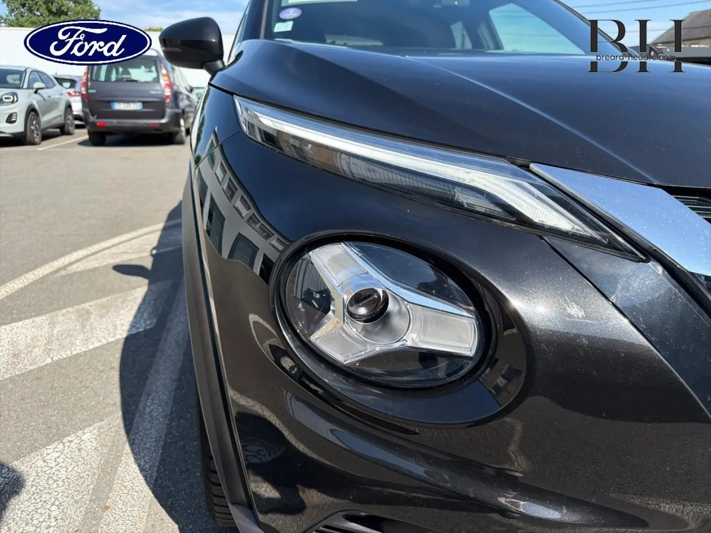 Gros plan sur le phare avant droit du Nissan Juke noir métallisé, mettant en valeur son design distinctif et moderne.