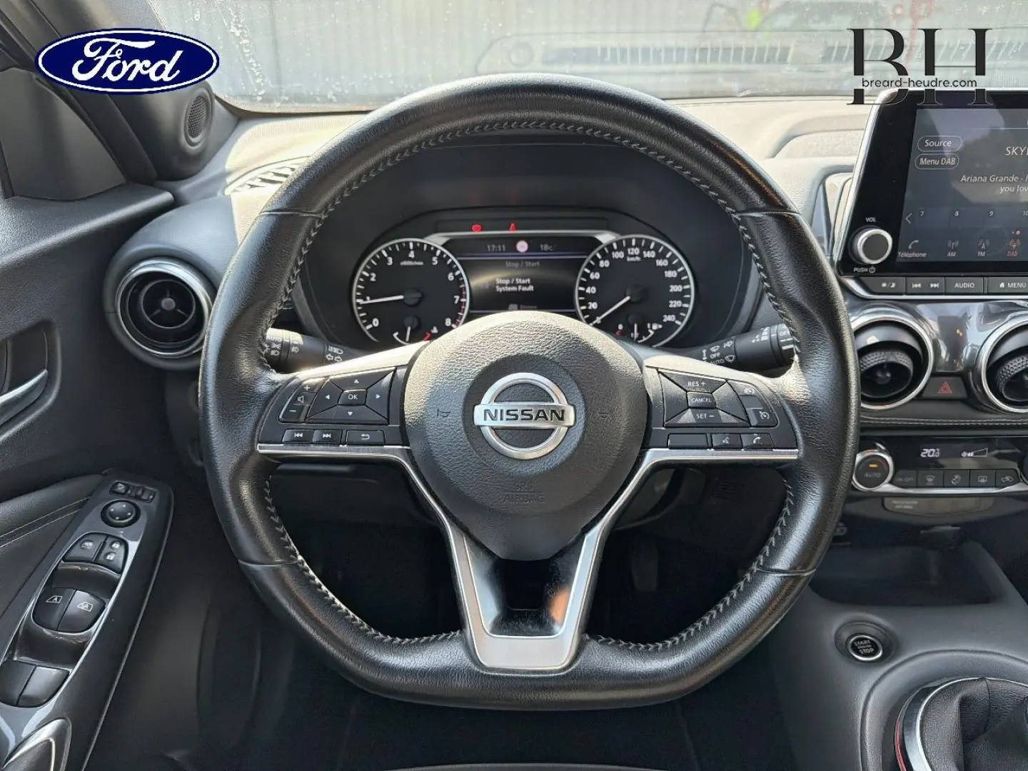 Vue intérieure centrée sur le volant cuir Nissan avec commandes multifonctions et tableau de bord digital.