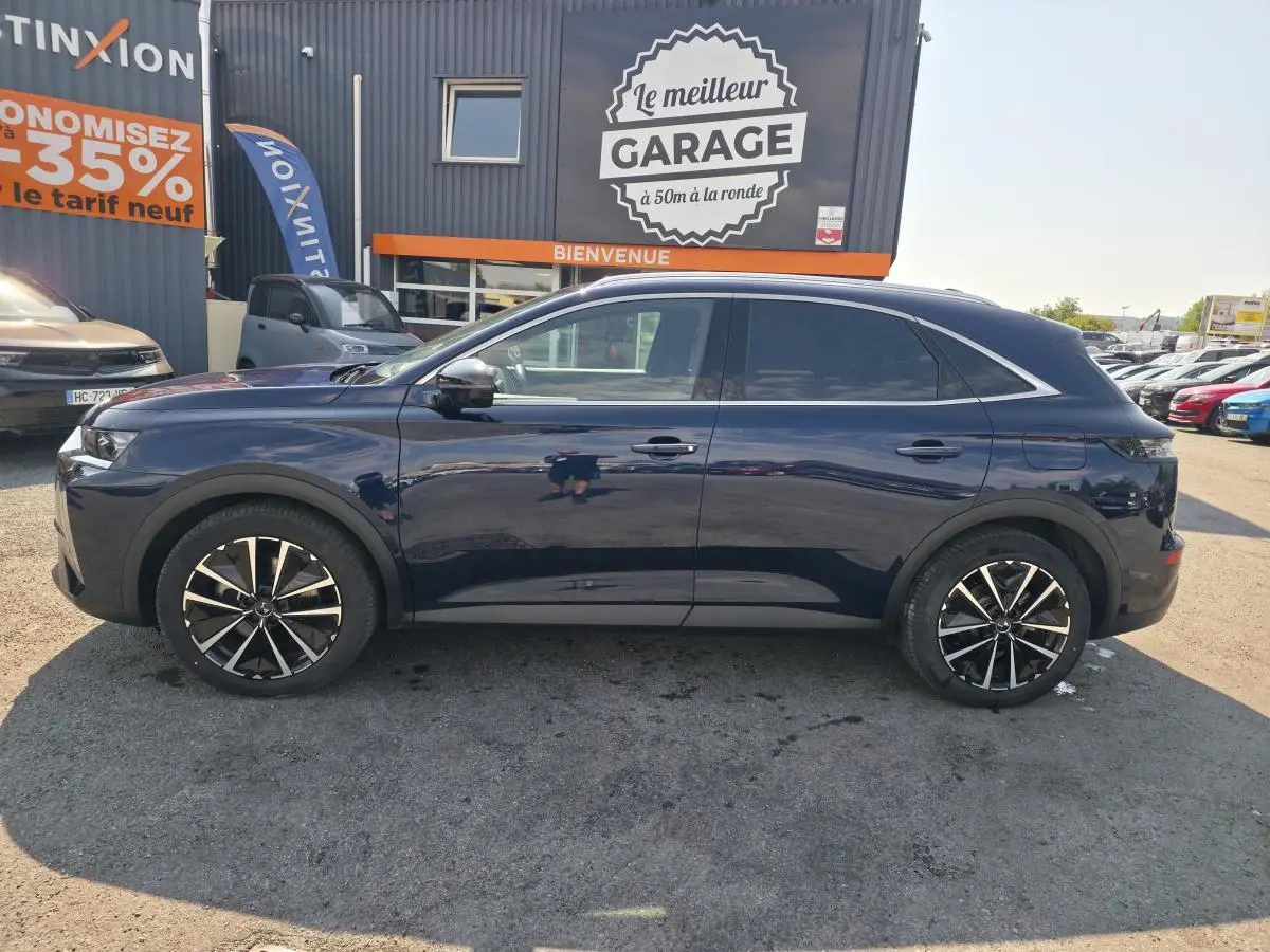 Vue latérale droite du SUV DS7 Crossback E-Tense 225 bleu métallisé avec jantes alliage 19 pouces, stationné devant un garage.
