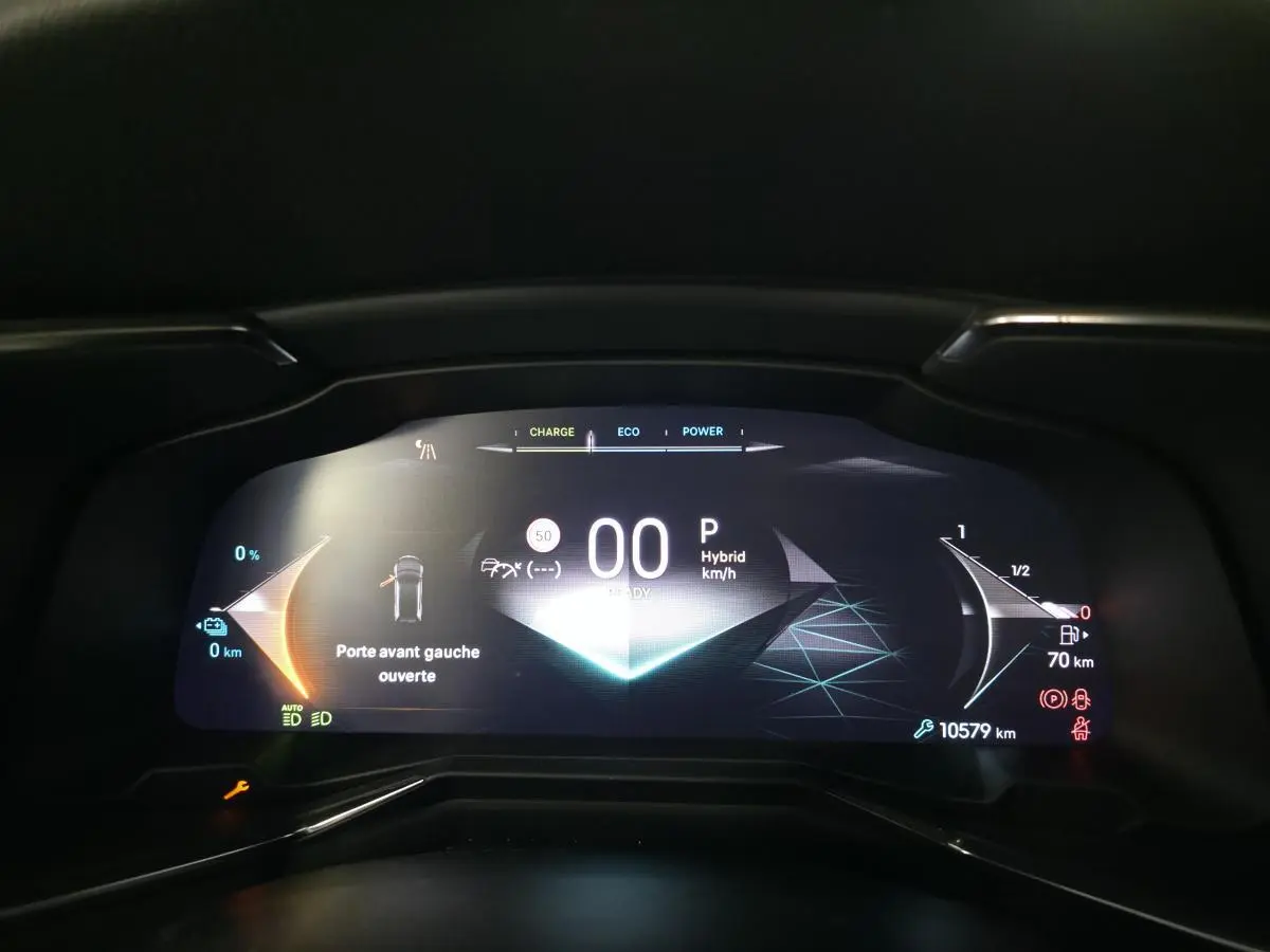 Tableau de bord numérique du DS7 Crossback E-Tense 2024 affichant vitesse, mode hybride et porte avant gauche ouverte.
