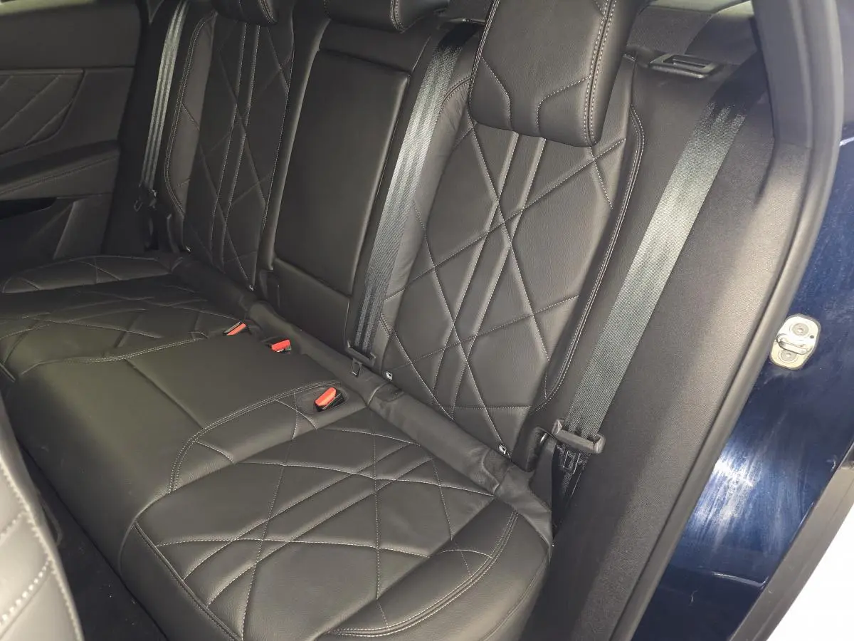 Vue rapprochée de la banquette arrière en cuir noir avec surpiqûres, porte arrière bleu visible sur le côté droit.