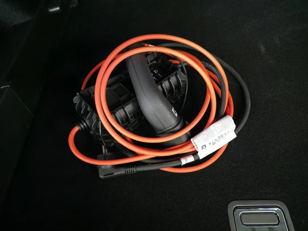 Câble de recharge hybride orange et noir enroulé dans le coffre d'un DS7 Crossback bleu.