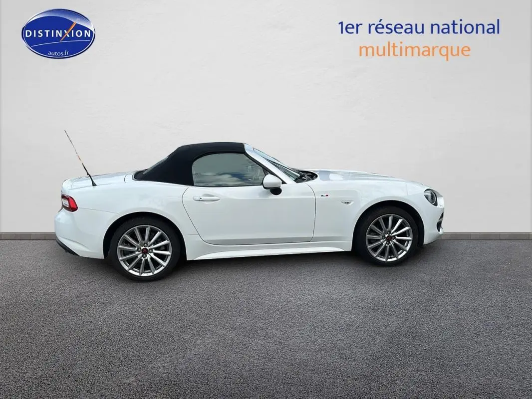 Profil côté gauche d'une FIAT 124 Spider blanc avec capote noire et jantes alliage 17 pouces sur fond neutre.