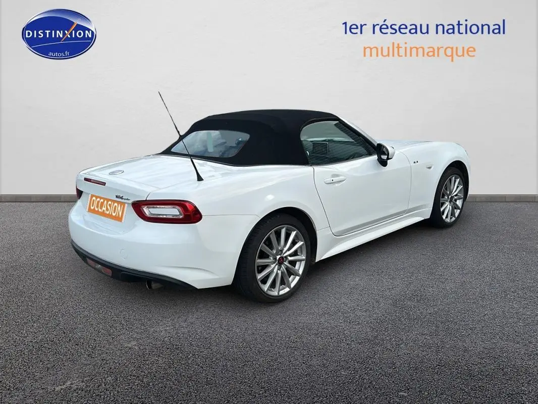 Fiat 124 Spider blanc vue 3/4 arrière droit avec capote noire et jantes alliage 17 pouces.