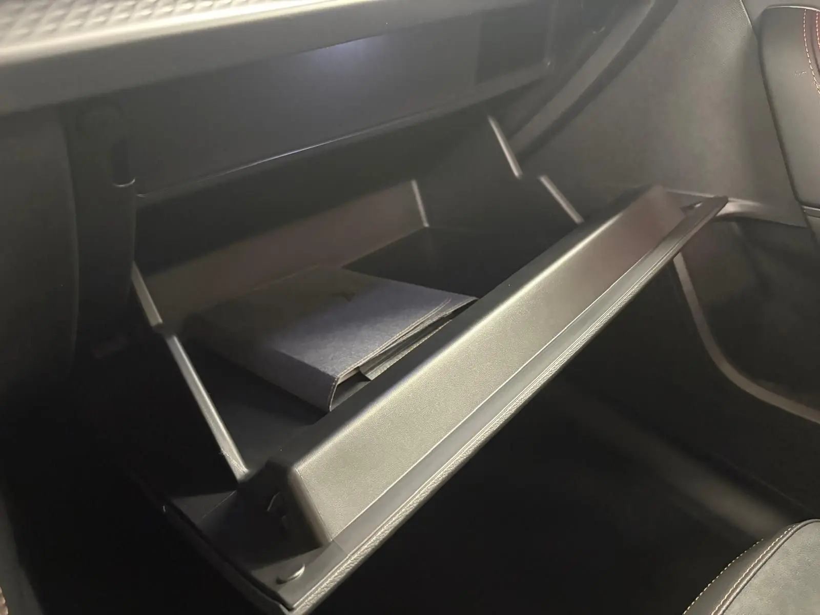 Gros plan sur la boîte à gants ouverte du CUPRA Formentor 2025, avec un livret à l'intérieur et sellerie noire.