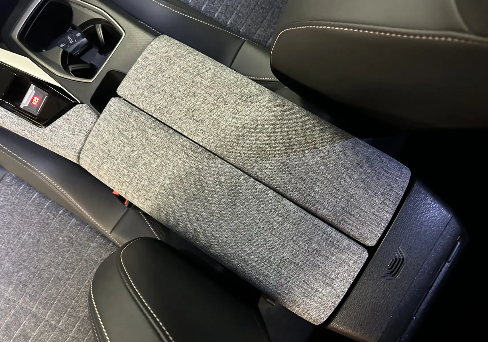 Détail de l'accoudoir central en tissu gris et cuir noir avec surpiqûres dans l'habitacle du Peugeot 3008 III Hybrid 145 e-DSC6 Allure.