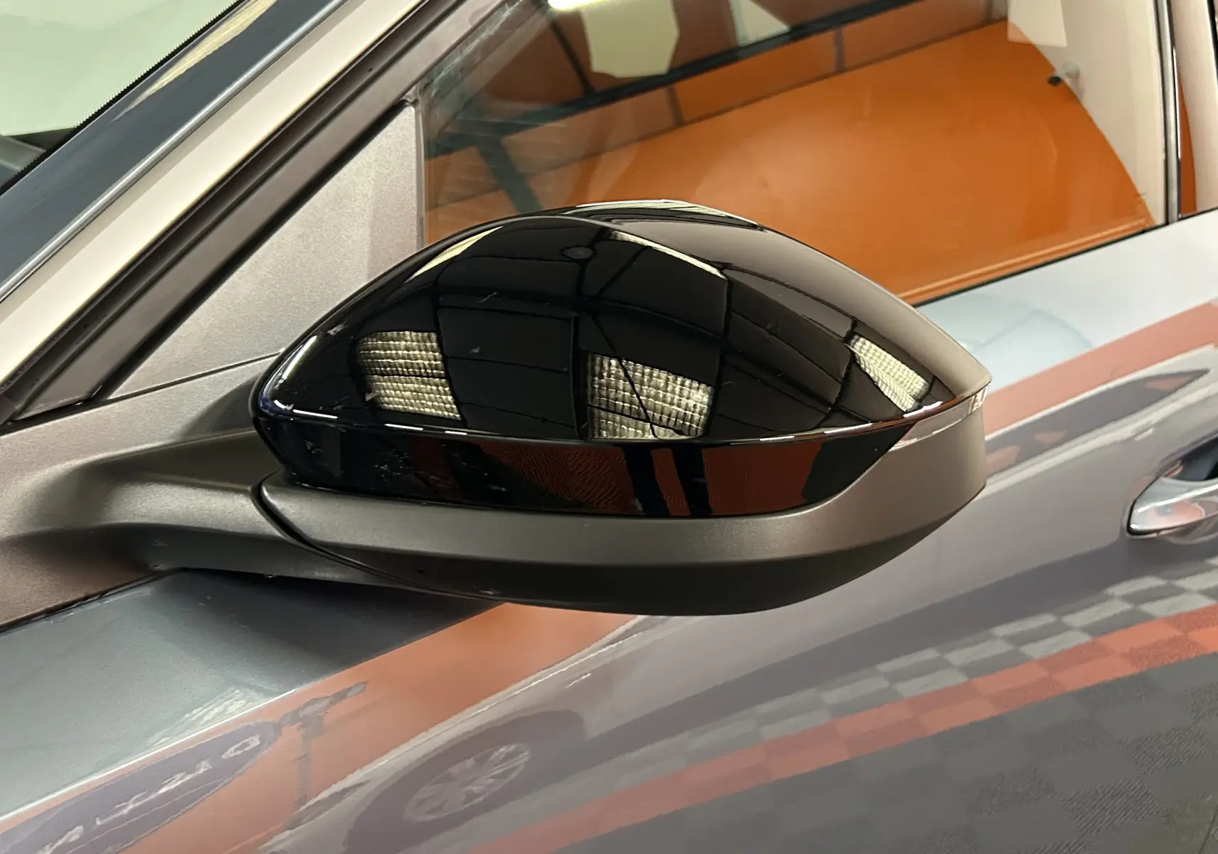 Rétroviseur noir brillant côté gauche du Peugeot 3008 III HYBRID 145 e-DSC6 Allure Bleu Ingaro avec reflet intérieur orange.