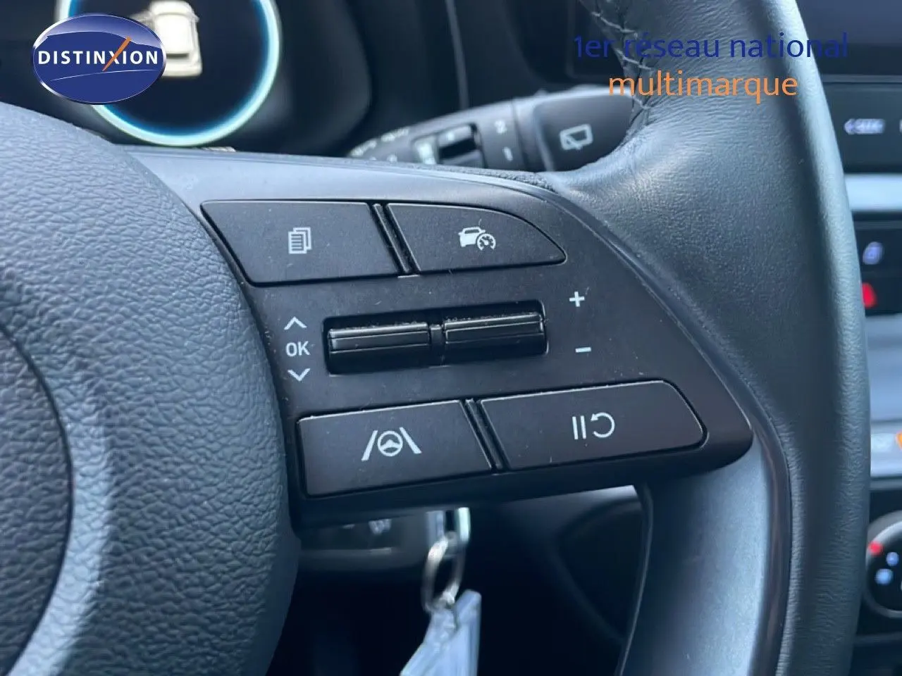 Gros plan sur les commandes au volant en cuir noir de la Hyundai i20 blanche, mettant en valeur les boutons de régulateur de vitesse.