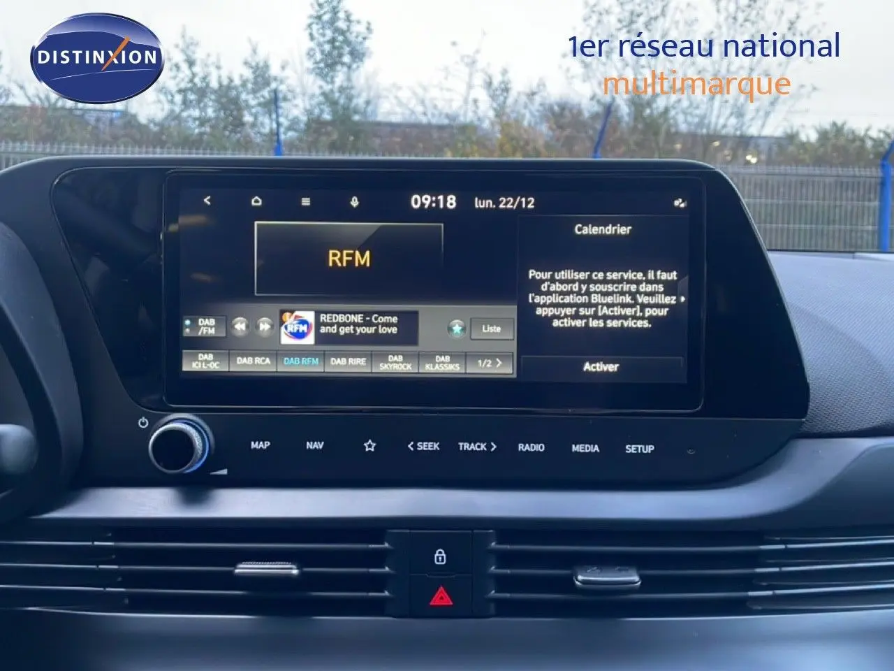 Vue intérieure centrée sur l'écran tactile multimédia de la Hyundai i20 blanche, affichant la radio et le calendrier.