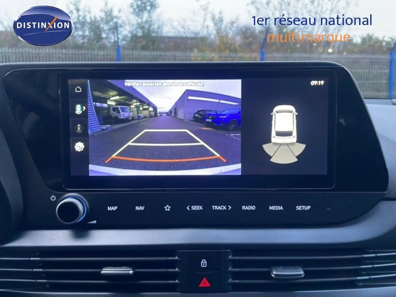 Écran tactile intérieur montrant la caméra de recul et l’aide au stationnement de la Hyundai i20 blanche, vue de face.
