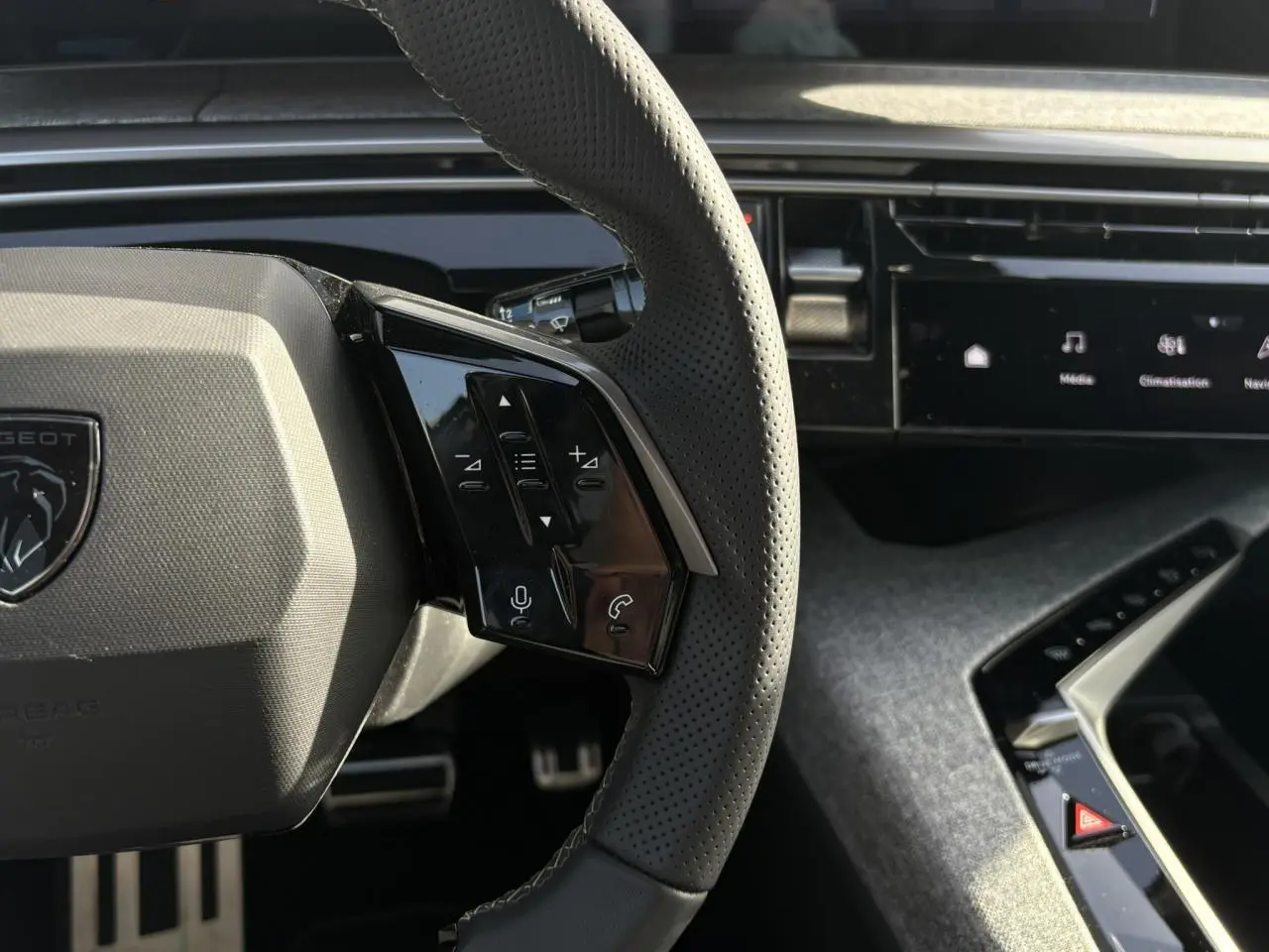 Gros plan sur le volant perforé noir avec commandes intégrées et partie de la planche de bord du Peugeot 3008 Hybrid 2025.