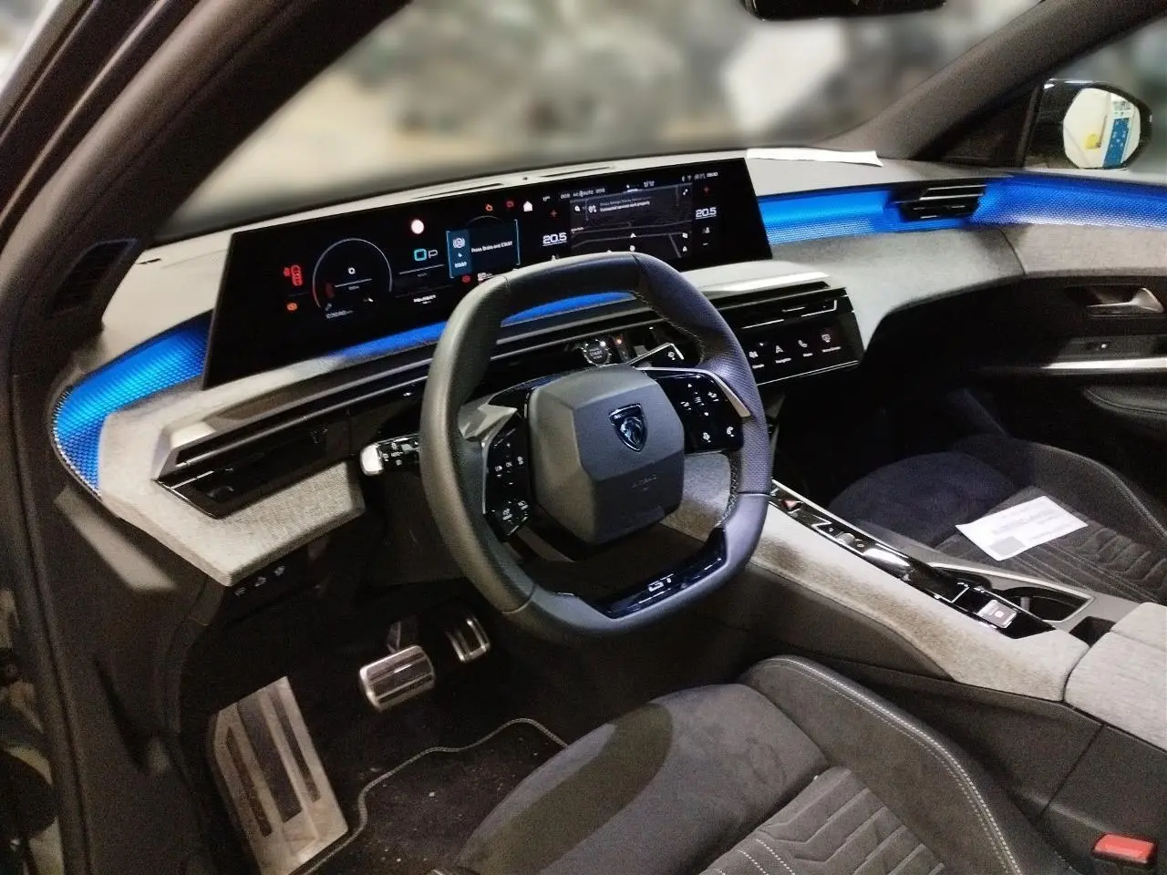 Vue intérieure côté conducteur du Peugeot 3008 Hybrid 145 e-DSC6 GT, tableau de bord avec éclairage bleu et volant compact noir.