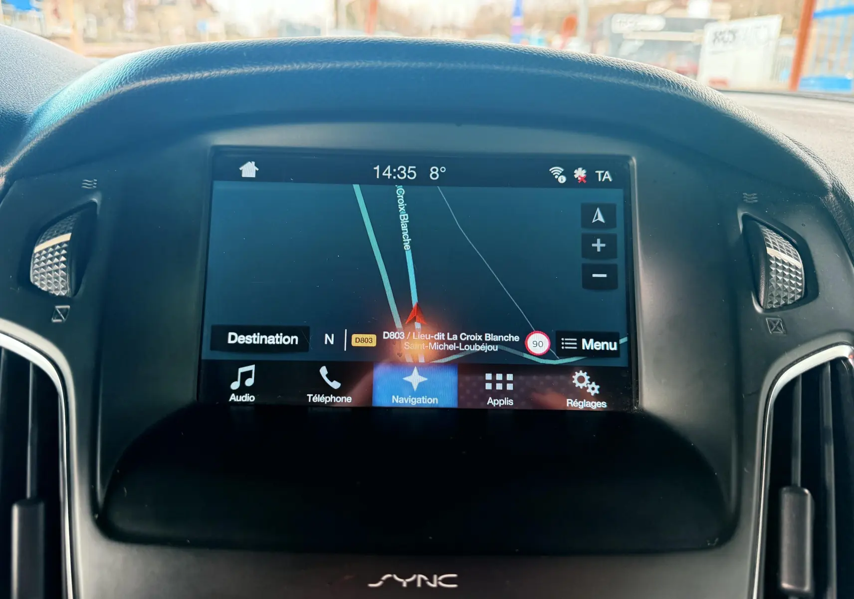 Vue intérieure du poste de conduite de la Ford Focus 1.5 TDCI gris, avec volant multifonction et écran tactile central allumé.