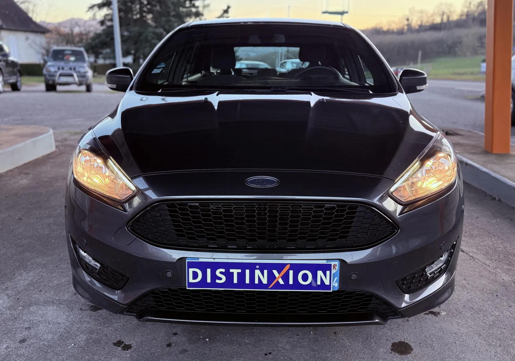 Vue avant d'une Ford Focus 1.5 TDCI 120 ST Line grise avec phares allumés et calandre noire distinctive.