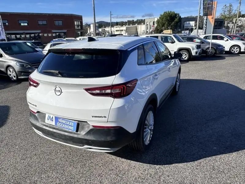 Vue 3/4 arrière droite d'un Opel Grandland X blanc de 2018, version 1.6 D 120 Innovation, sur parking extérieur.