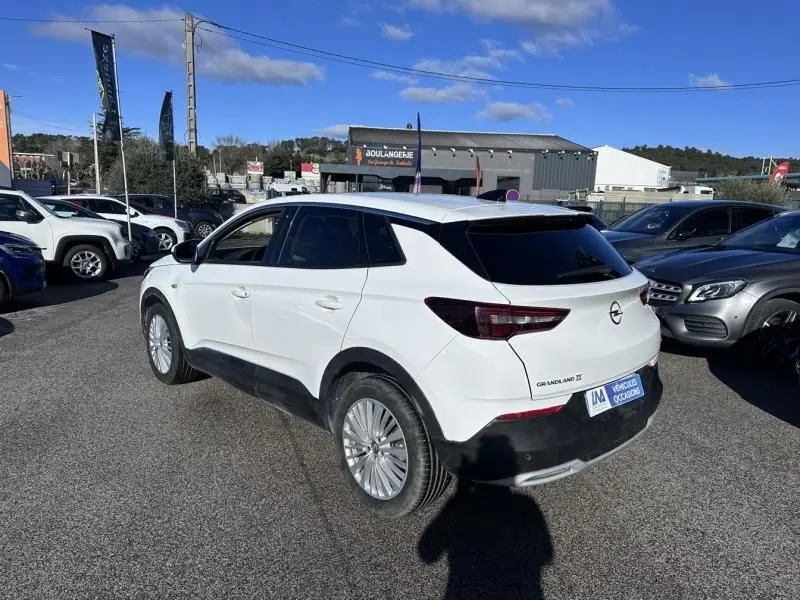 Vue 3/4 arrière droite d’un Opel Grandland X blanc 2018, avec vitres teintées et jantes alliage, stationné en extérieur.