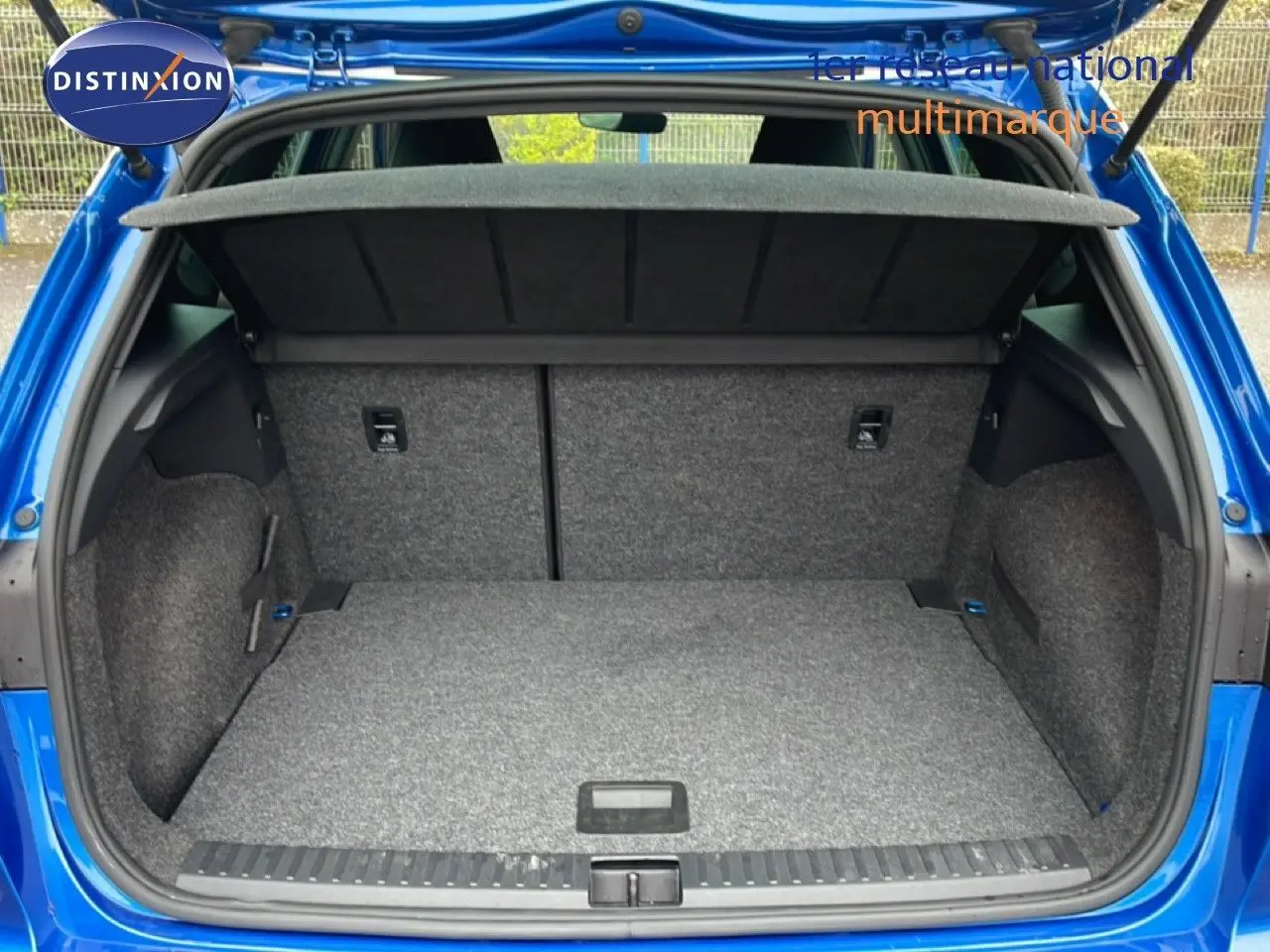 Coffre ouvert vu de l'arrière d'une SEAT Arona bleu saphir métal, montrant l'espace de chargement vide.
