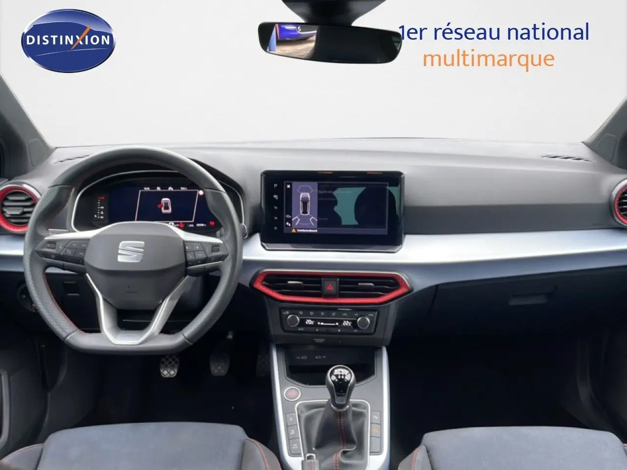 Vue intérieure avant du tableau de bord du SEAT Arona 2025 avec volant multifonction et touches rouges autour des aérateurs.