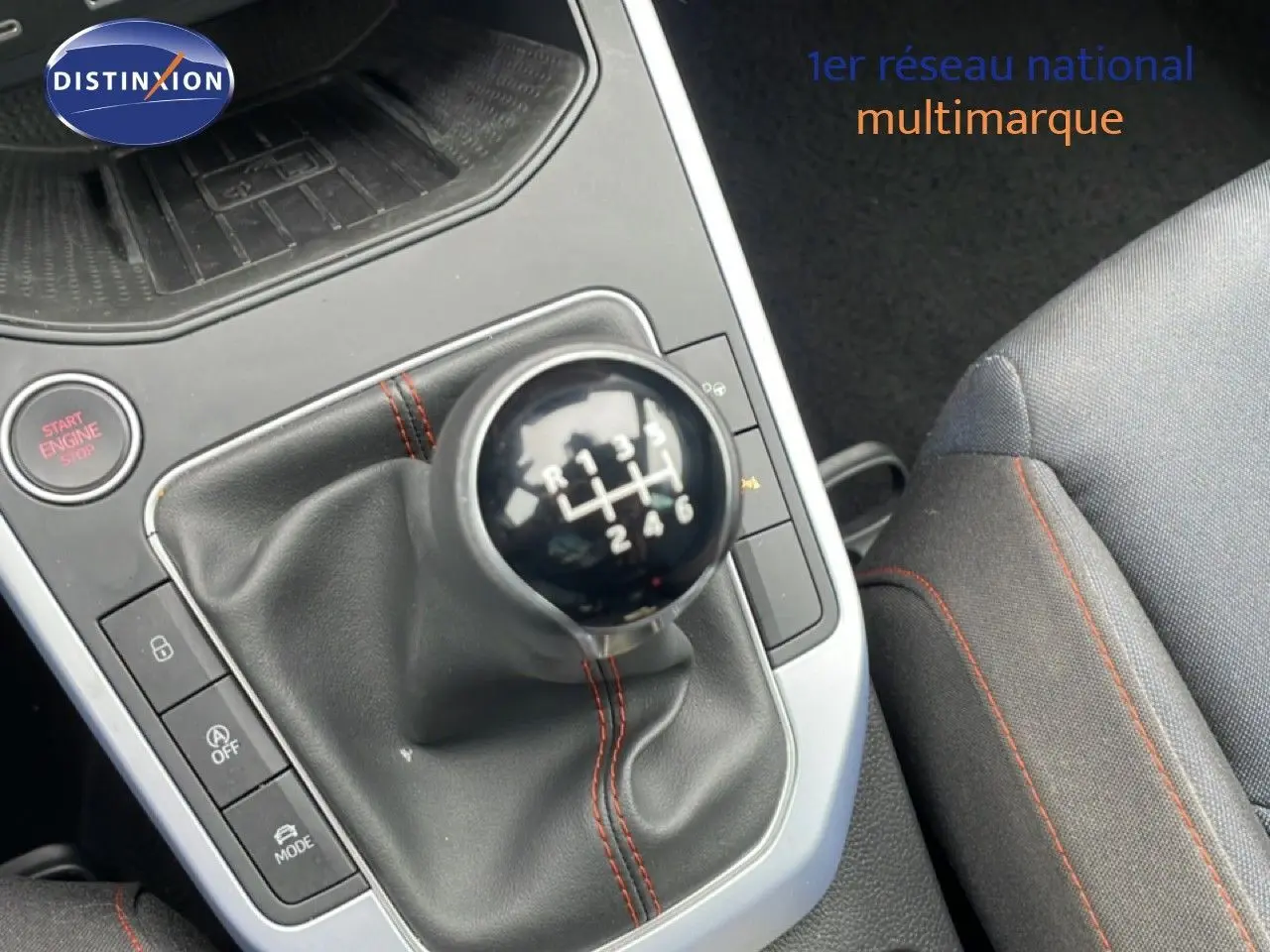 Gros plan sur le levier de vitesses manuel avec coutures rouges, siège tissu gris et bouton Start Engine dans un SEAT Arona 2025.