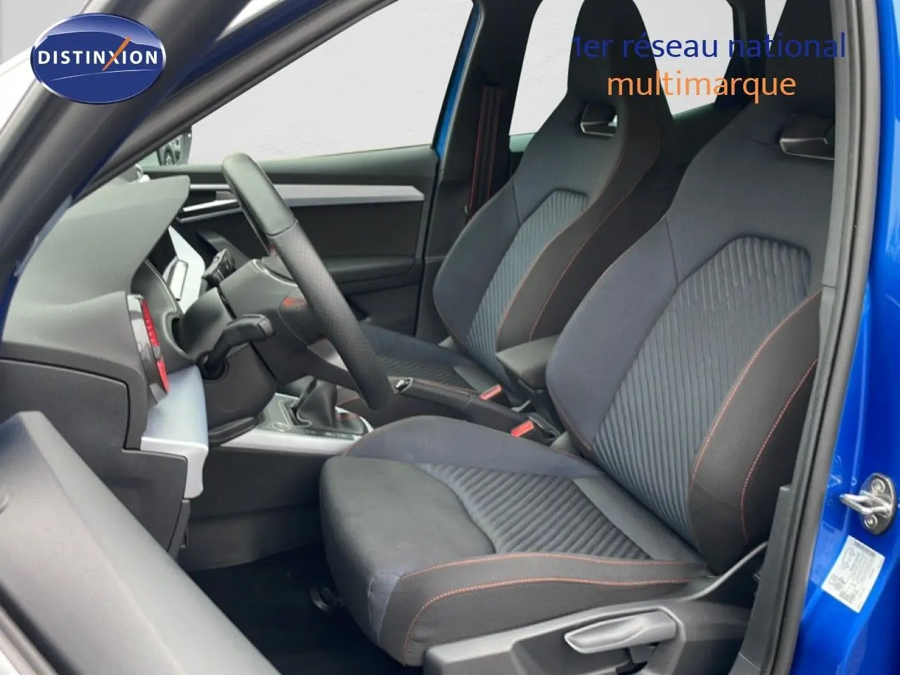 Vue intérieure côté conducteur du SEAT Arona bleu saphir, sièges sport tissu noir avec surpiqûres orange.