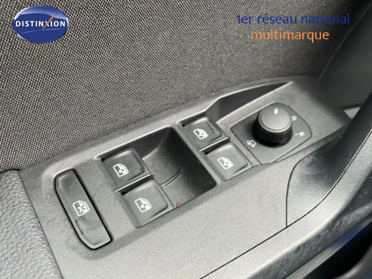 Gros plan sur les commandes des vitres électriques et réglage des rétroviseurs côté conducteur d'une SEAT Arona bleu saphir toit blanc.