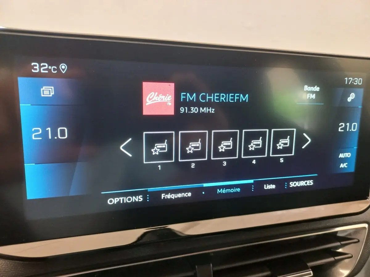 Écran tactile central du Peugeot 3008 noir, affichant la radio FM et la température intérieure à 21°C.