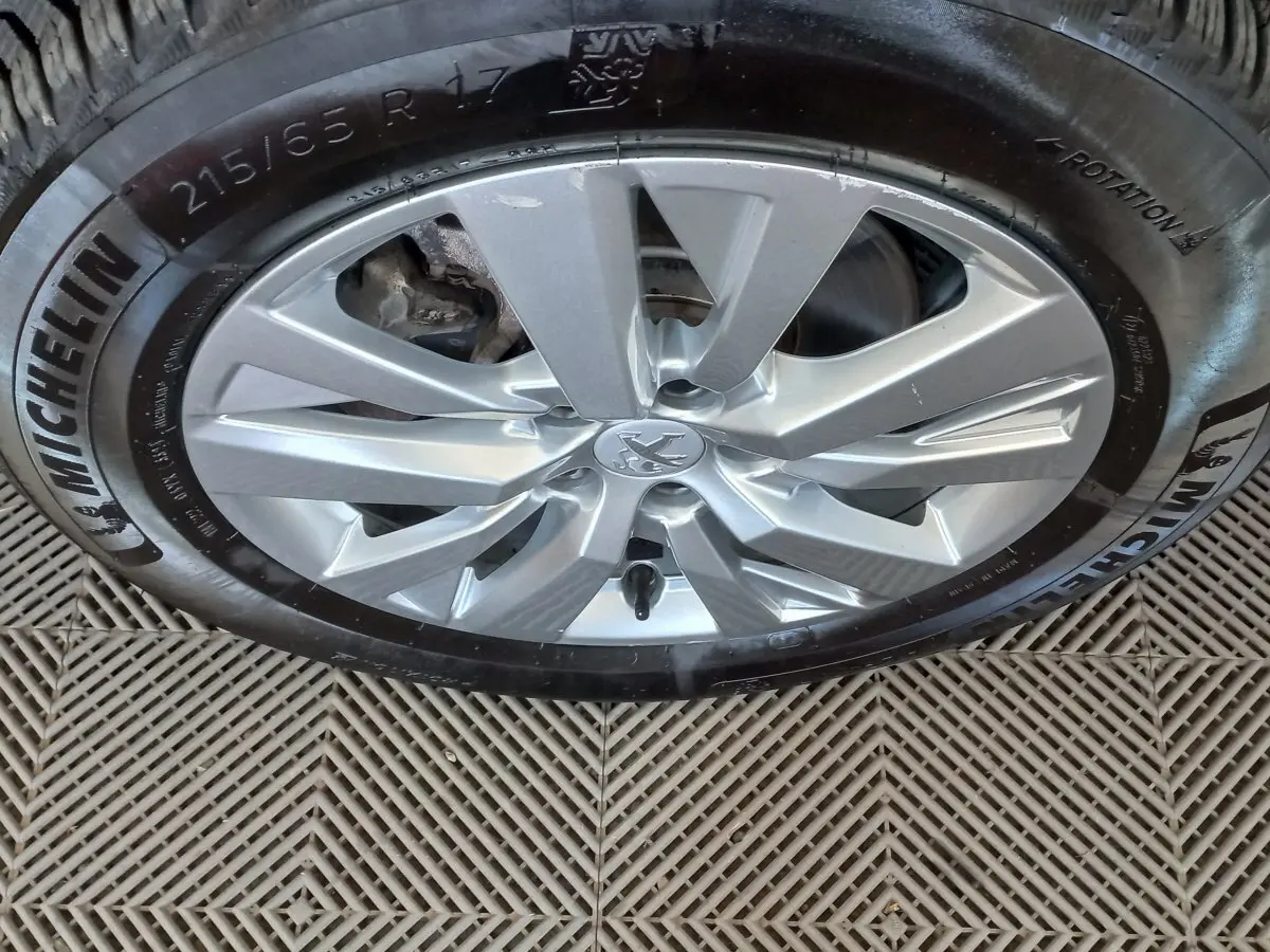 Gros plan sur la roue avant droite du Peugeot 3008 noir, jante alliage argentée avec logo Peugeot central.