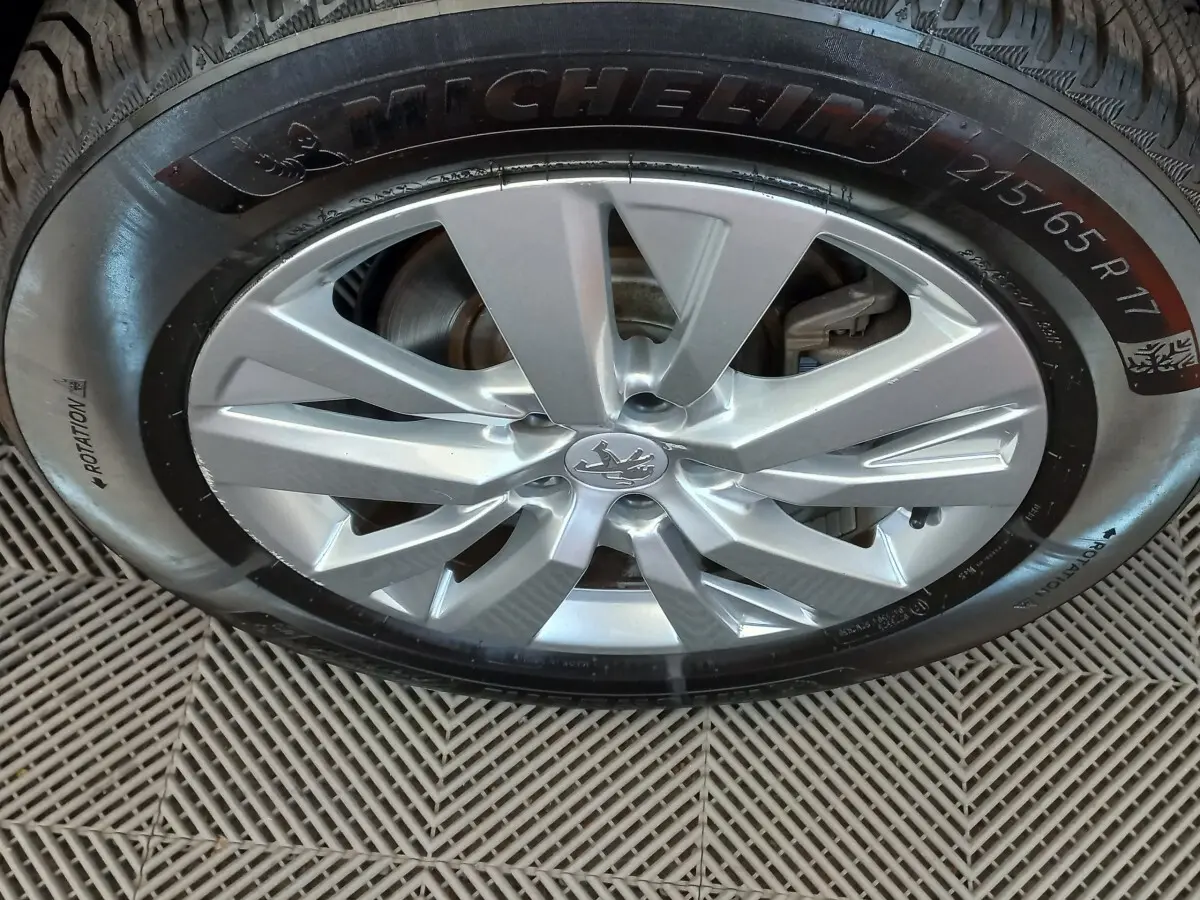 Gros plan sur la jante alliage argentée avec logo Peugeot, montée sur pneu Michelin 215/65 R17.